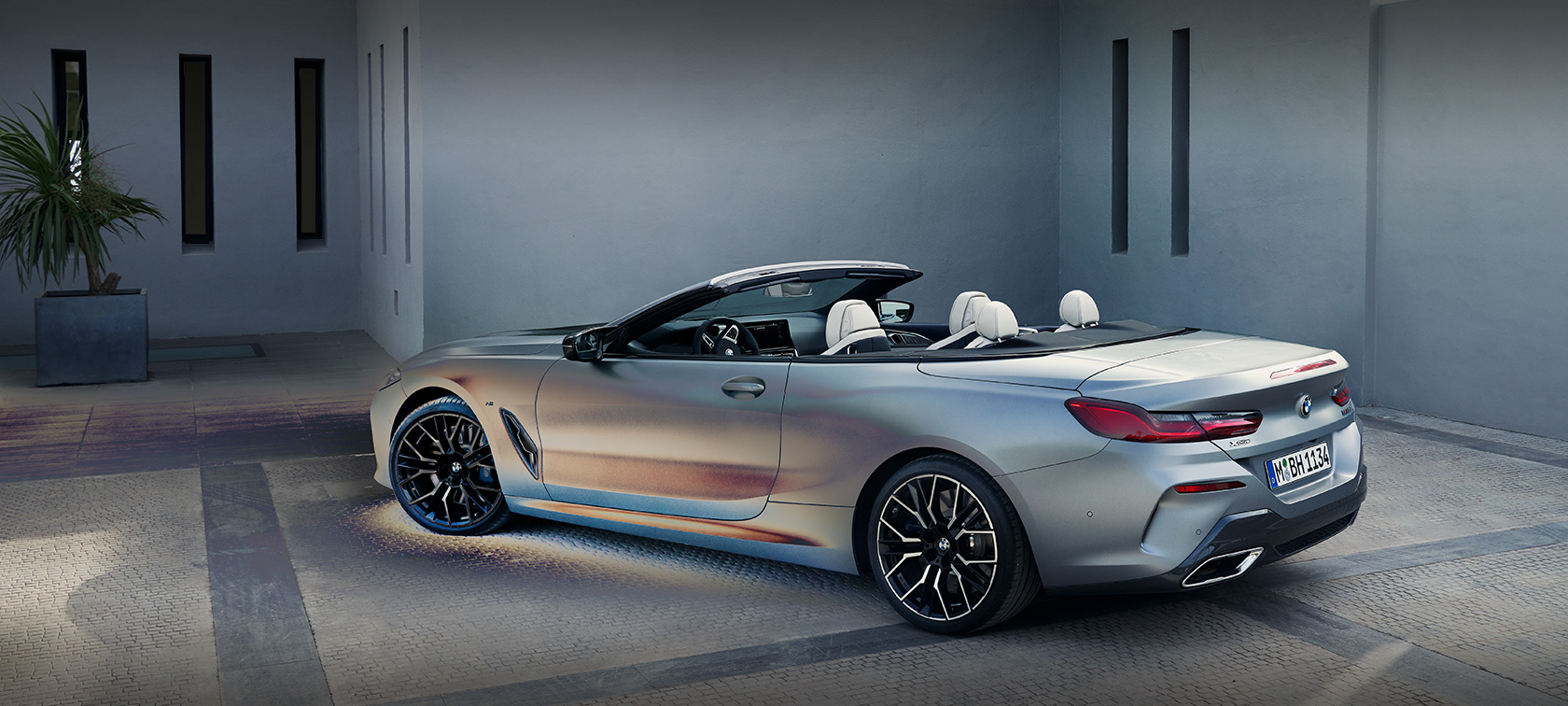 Man leaning against The New BMW 8 Series Convertible G14 LCI Facelift 2022 BMW Individual Frozen Pure Grey metallic side view standing in front of a building with male model