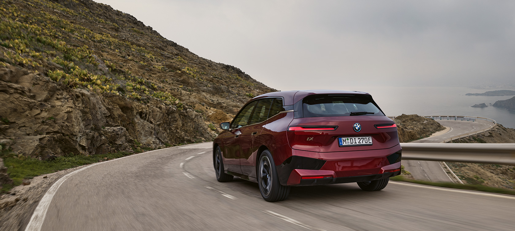 BMW iX i20 2021 electric SUV BMW iX xDrive50 Aventurin Red rear view driving on coastal road