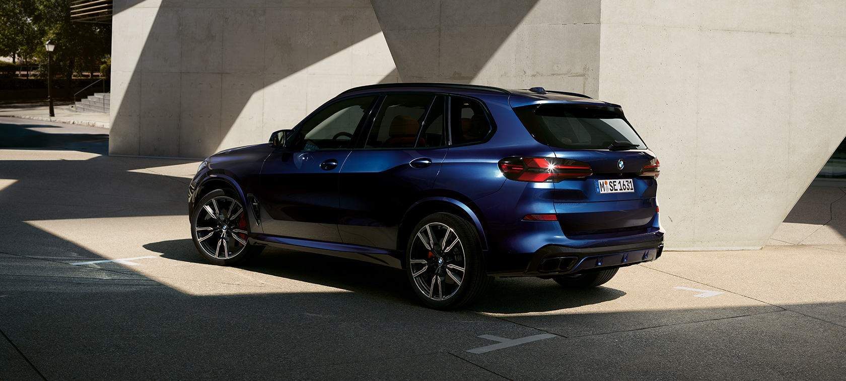 BMW X5 M60i xDrive G05 MP three-quarter rear view standing in front of building with light incidence