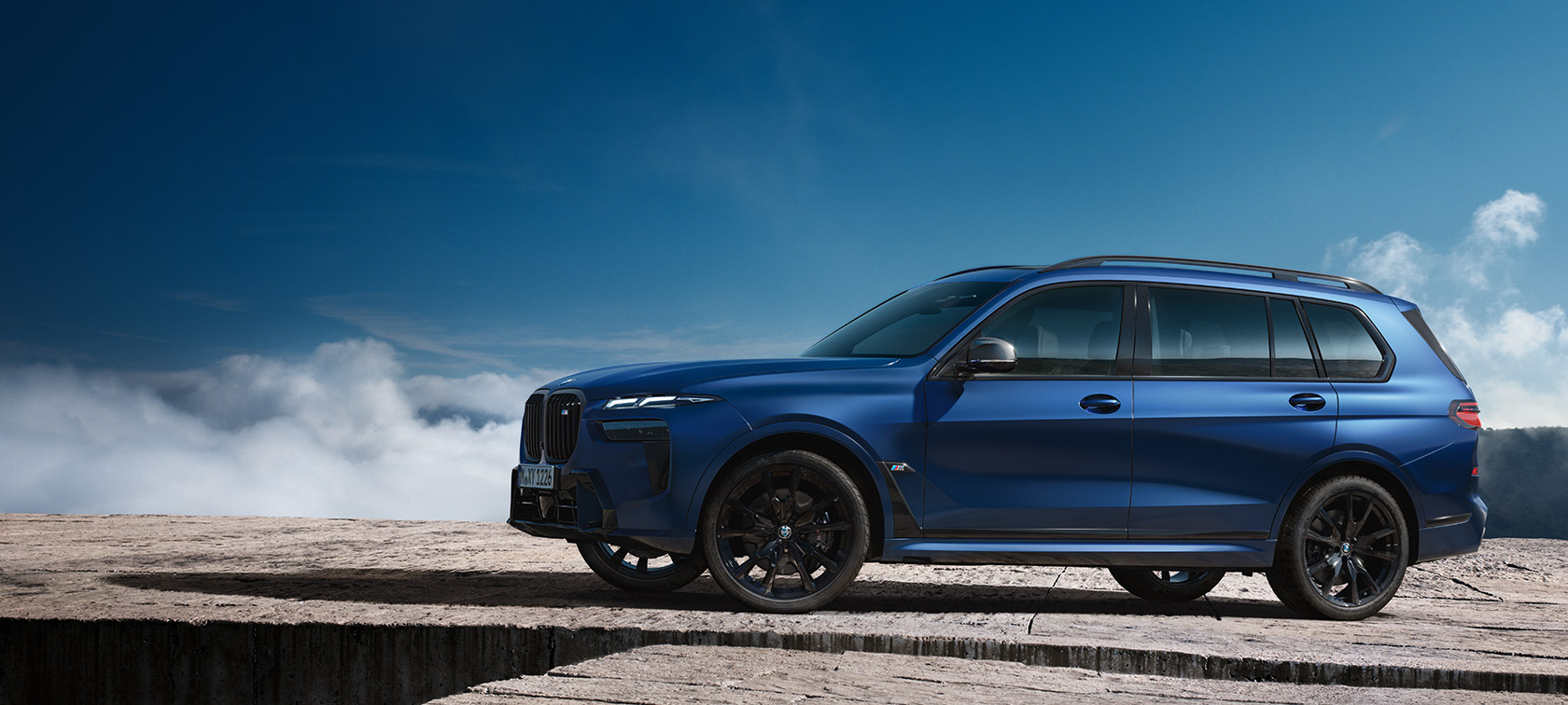 BWM X7 M60i xDrive G07 LCI Frozen Marina Bay Blue side view standing in front of mountain landscape 